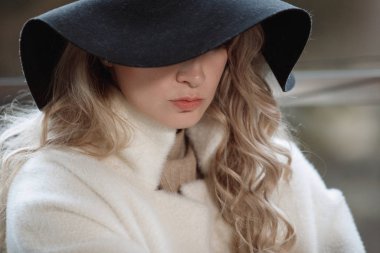 Siyah şapkalı, uzun saçlı, bej ceketli sarışın bir kadının portresi..