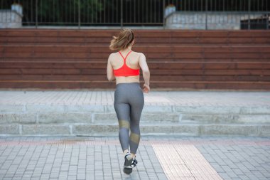 Turuncu bluzlu bir kadın yazın şehir parkında kaldırımda koşar. Arka plan.