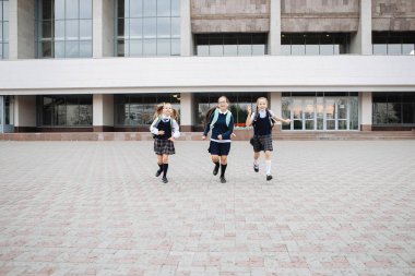 Üniformalı üç öğrenci neşeli ve neşeli bir şekilde okuldan kaçıyorlar..