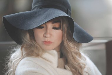 Siyah şapkalı, uzun saçlı, bej ceketli sarışın bir kadının portresi..