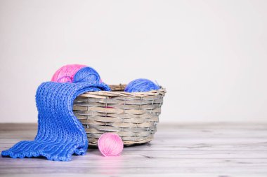 İçinde yün toplar ve mavi ve pembe el örgüsü eşarplar olan sepet. Gri arkaplan.