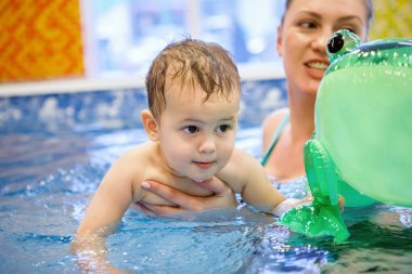 Tatlı bebek havuzda yüzmeyi bir eğitmenin yardımıyla öğreniyor..