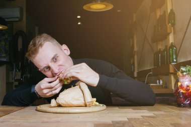 Genç sarışın adam kafedeki bir masada sandviç yemekten hoşlanıyor..