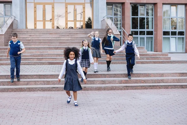 African girl and schoolchildren in uniform joyfully run out the stairs in front of the school.