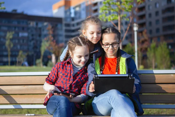Trzy Nastolatki Smartfonem Tabletem Siedzące Latem Ławce Parku Miejskim — Zdjęcie stockowe