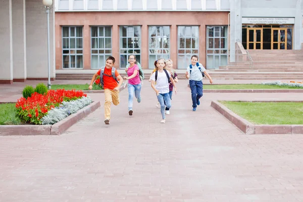 Group of schoolchildren with backpacks runs out of school after lesson.