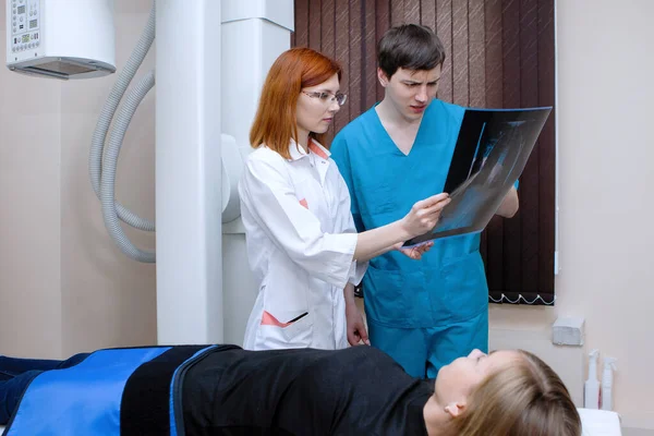 女性と男性の放射線技師は 医療室で患者の近くのX線を検査します — ストック写真