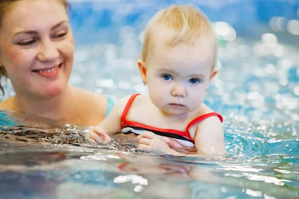 Woman child trainer and toddler swim and study in blue water pool