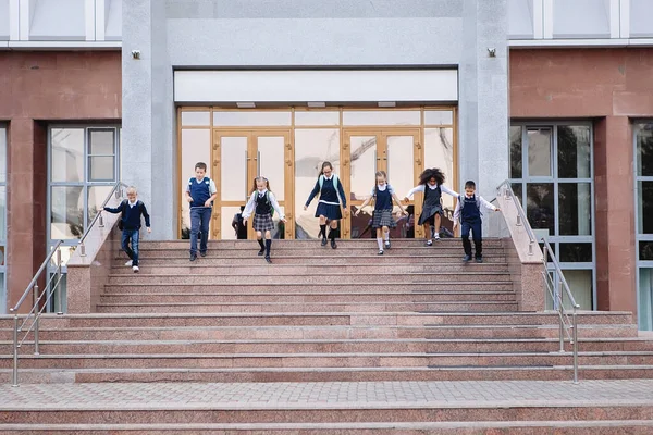 Group of schoolchildren in uniform are running down the stairs out of school.