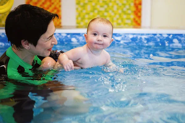 Woman child trainer and toddler swim and study in blue water pool