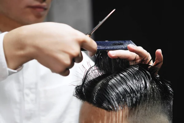Young guy hairdresser cuts hair with scissors to a man in a beauty salon.