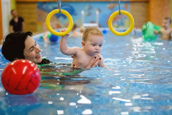 Woman coach teaches toddler to swim in the pool with gymnastic rings.