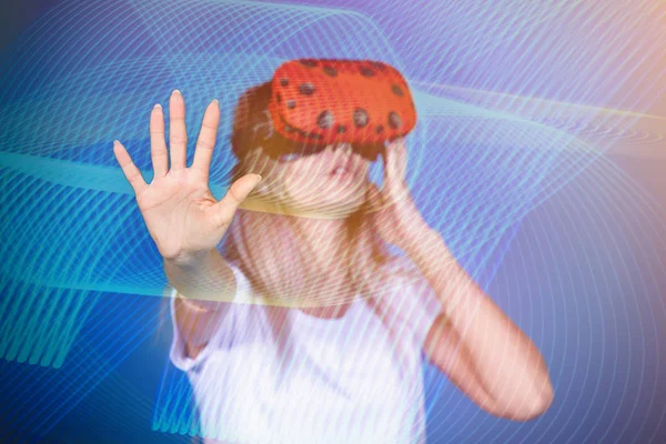 Young woman shows her hand stop in virtual reality glasses. Computer games, blue background, emotions.