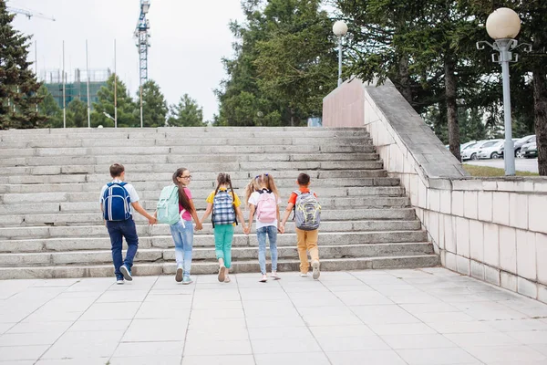 バックパック付きのカラフルな服を着た子供たちは学校への階段を歩いています バックビュー — ストック写真