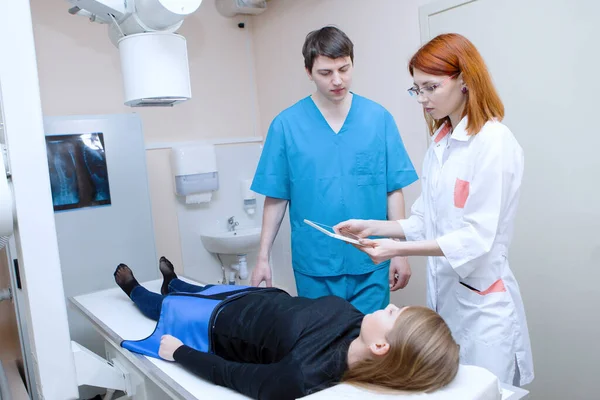 女性と男性の放射線技師が診療所の患者の近くのタブレットでX線を検査しています — ストック写真
