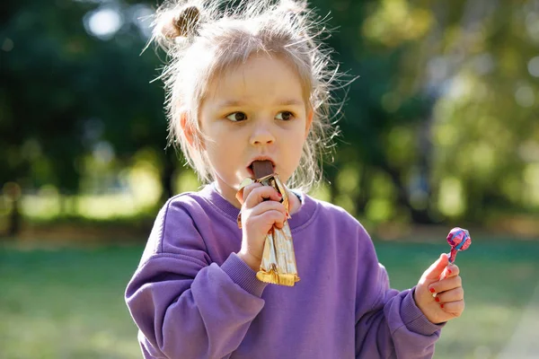 Klein Meisje Een Paars Pak Eet Chocolade Een Stadspark Zomer — Stockfoto