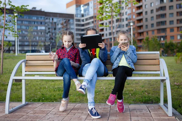 Tres Adolescentes Con Teléfono Inteligente Tableta Sentados Banco Parque Ciudad —  Fotos de Stock