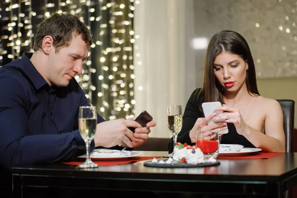 Couple at a table in a restaurant looking at smartphones. Technology versus human communication