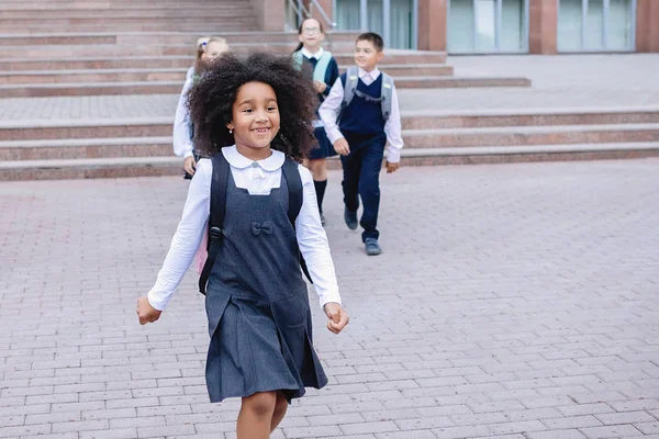 African girl and schoolchildren in uniform joyfully run out the stairs in front of the school.