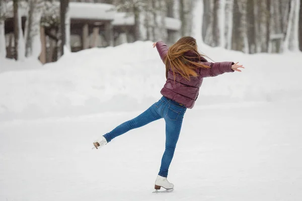 若い女の子は屋外の冬の公園のアイスリンクでスケートをしています 暖かい服 ニット帽 雪のドリフト ぼやけた背景 — ストック写真