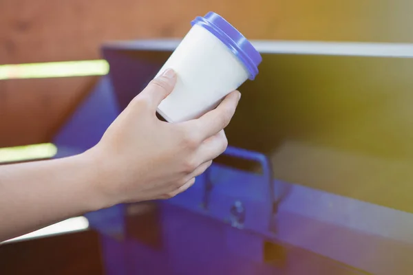 Female hand throwing a plastic cup into a trash can.