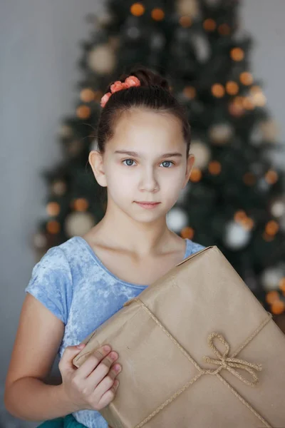 Genç Kız Elinde Hediye Kutusuyla Bir Noel Ağacının Yanında Oturuyor — Stok fotoğraf