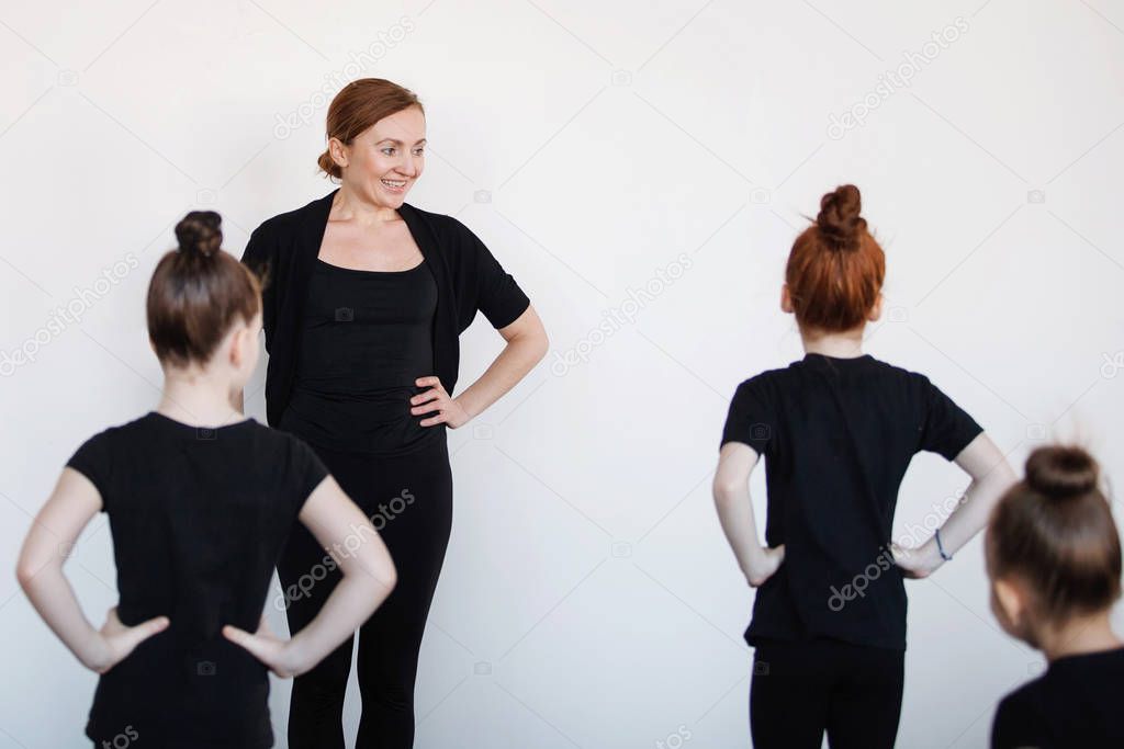 Group of teenage girls dancers in a lesson with a trainer. Black leotard, hair in a bun, white socks.