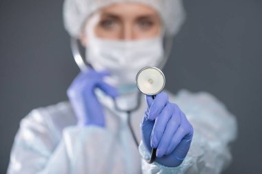 Steteskoplu, koruyucu maskeli, şapkalı, silikon eldivenli bir doktor..