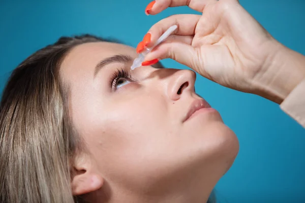Woman drops eyedrops in her eyes to treat a disease.
