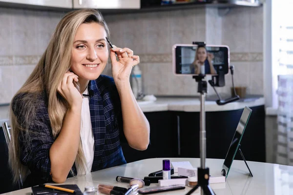Woman blogger does brow makeup on smartphone online. Coronavirus quarantine homework, social distance, private entrepreneur. Selected Focus.