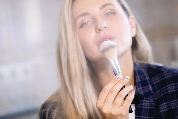 Woman shows a cosmetic brush with tonal powder.