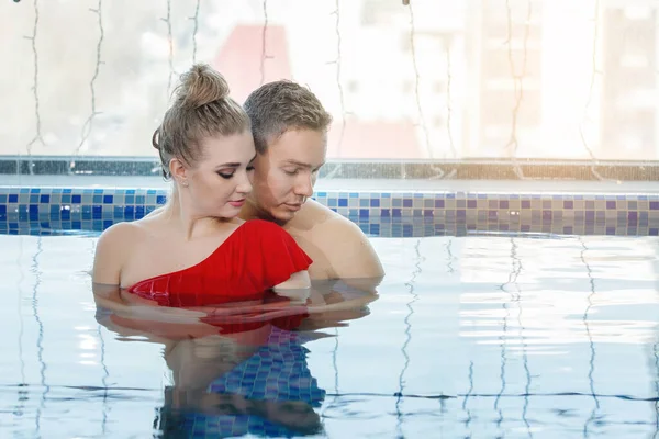年轻貌美的一对 男人和女人在游泳池里悠闲自在 她穿着红色游泳衣 蓝色的水 有选择的重点 背景模糊 — 图库照片