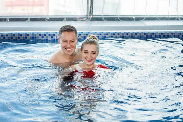 可爱的年轻夫妇 男人和女人在游泳池里放松一下 她穿着一件红色的泳衣 蓝色的水 有选择的重点 模糊的背景 — 图库照片