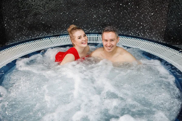 年轻貌美的夫妇正在按摩浴缸里放松 蓝色泡沫般的水 快乐的微笑 融合在一起 有选择的重点 模糊的背景 — 图库照片
