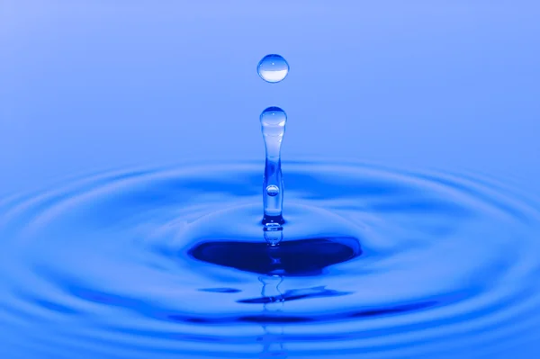 Капля падает и плещется на голубой поверхности воды — стоковое фото