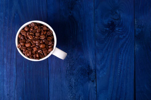Кружка полная кофейных зерен на синем деревянном фоне — стоковое фото