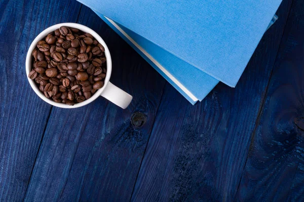 Кружка, полная кофейных зерен и двух голубых книг — стоковое фото