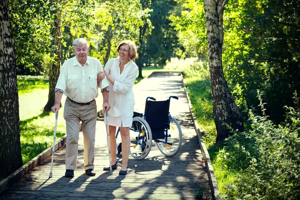 Old man with crutches and young woman in the park — Stock Photo, Image