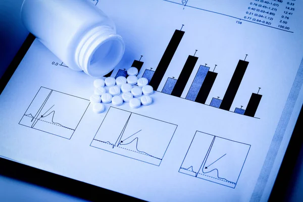 White pills and printed medical graphs — Stock Photo, Image