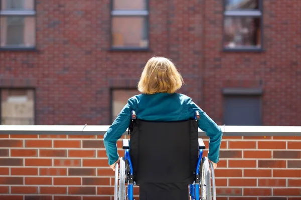 Femme seule en fauteuil roulant entourée de bâtiments en briques — Photo