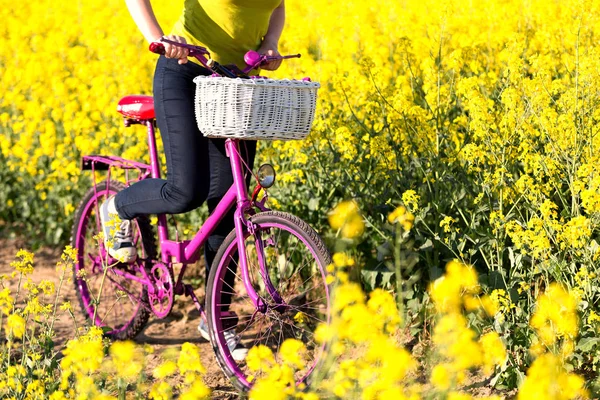 Dziewczyna z różowy rower w polu rzepaku — Zdjęcie stockowe