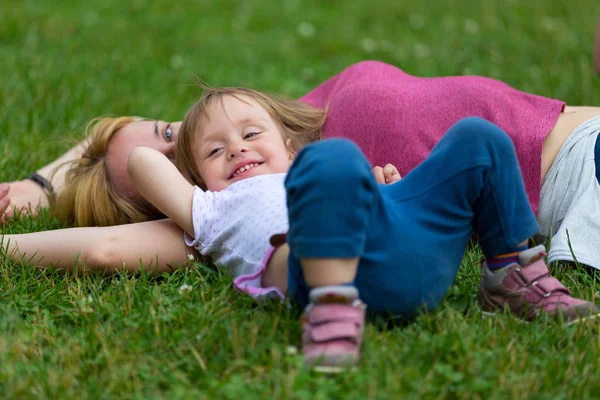Mała dziewczynka leżąc na trawie z matką — Zdjęcie stockowe