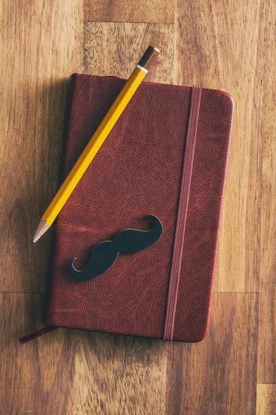 Fake black mustache on diary with pencil. — Stock Photo, Image