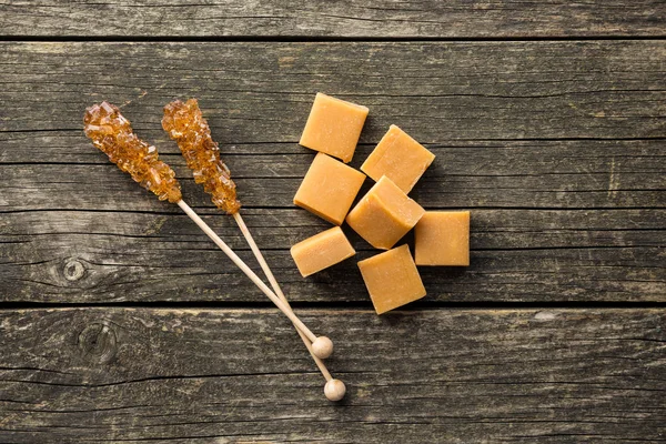 Brown sugar crystals on stick and caramel candies. — Stock Photo, Image