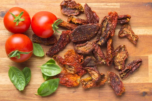 Tomates secos en rodajas y tomates frescos con hojas de albahaca . —  Fotos de Stock