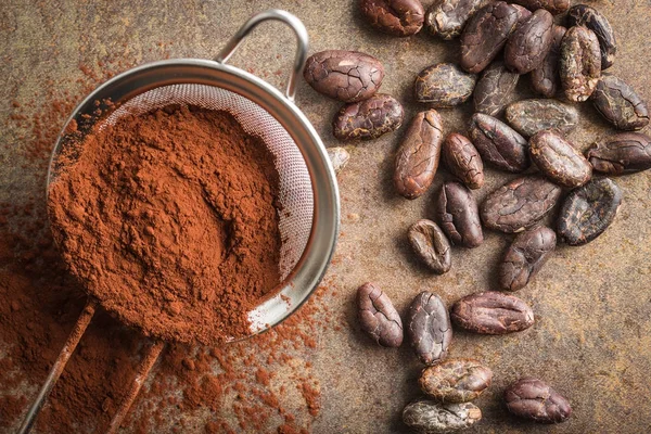 Donkere cacaopoeder in een zeef en cacaobonen. — Stockfoto