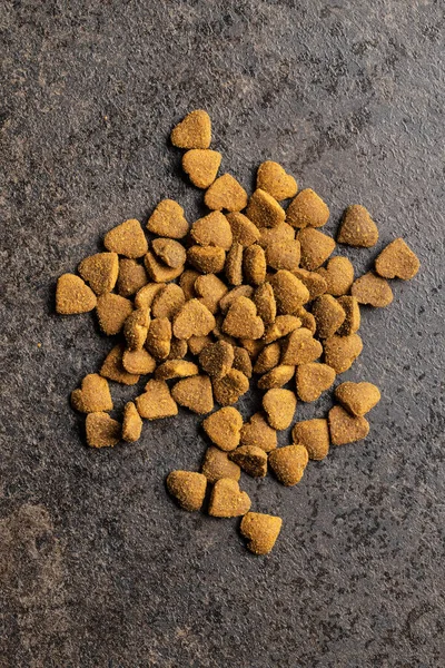 Dried kibble pet food. Heart shape dried animal food on old table. Top view.