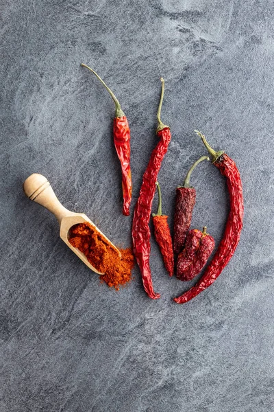Dried red chili peppers and chili powder spice in wooden scoop. Top view.