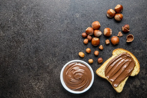 ヘーゼルナッツのトーストパンが広がります ブラックキッチンテーブルの上で甘いチョコレートクリーム トップ表示 — ストック写真