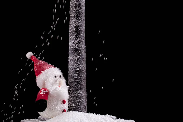 Père Noël sous un arbre avec de la neige sur fond noir — Photo